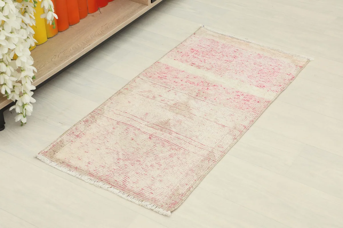 Angled view of the rose and ivory striped vintage rug, showing its rectangular shape and faded pattern.