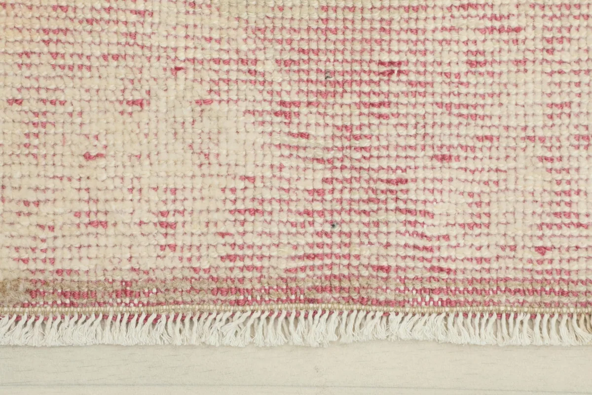 Close-up detail of the rose and ivory wool pile and short fringes of the vintage rug.