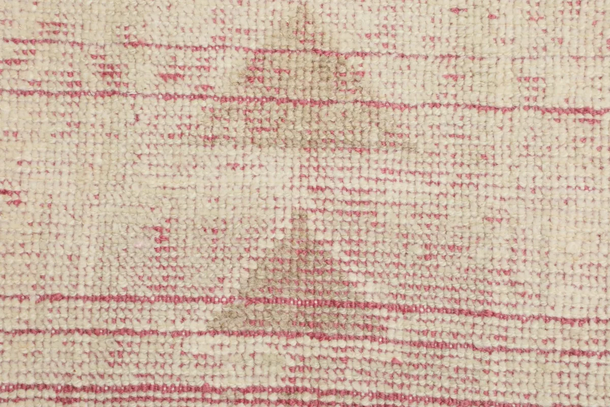 Close-up of the rug's surface, showing the subtle color variations and wear in the rose and ivory tones.