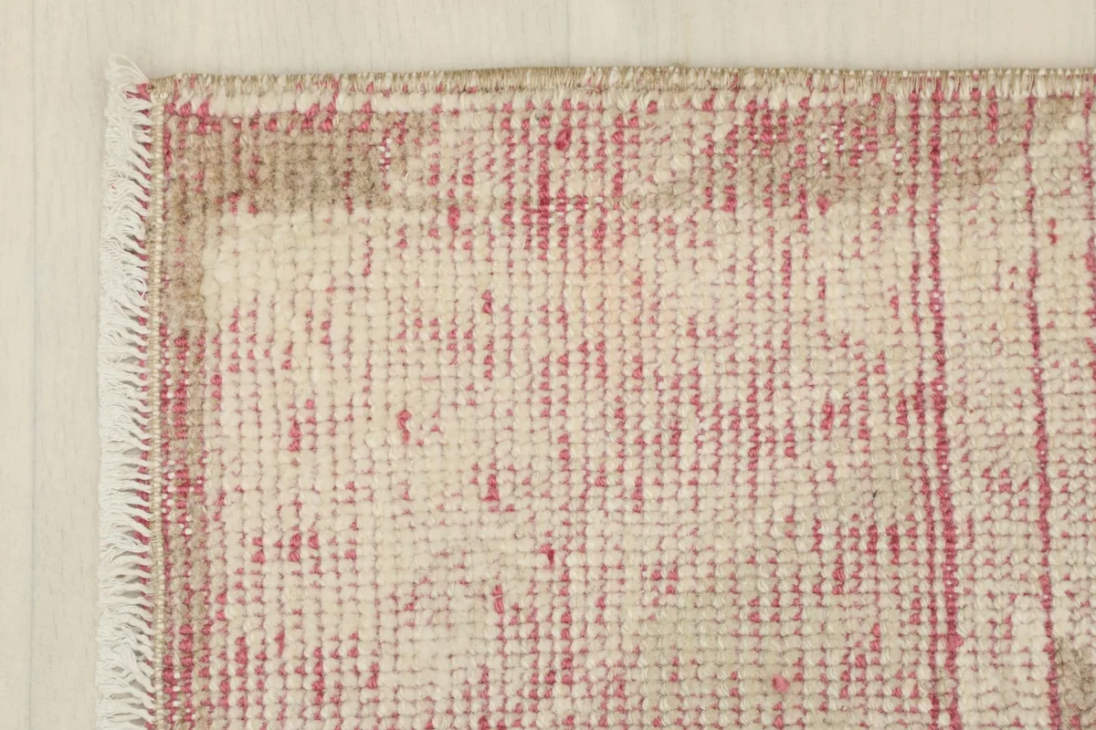 Corner detail of the rug, showing the edge finish and the blend of rose and ivory colors.