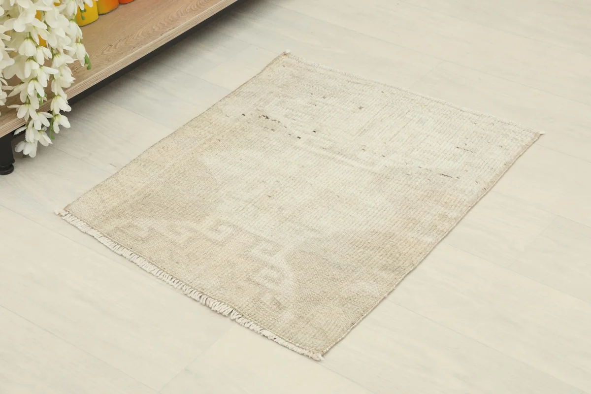 Angle view of the beige geometric doormat rug on a light floor, showing its small size