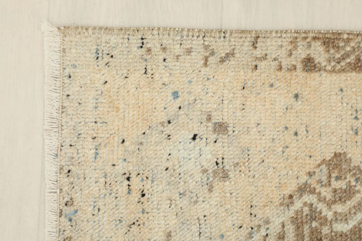 Close-up of the rug's corner showing beige field and subtle blue and charcoal speckles