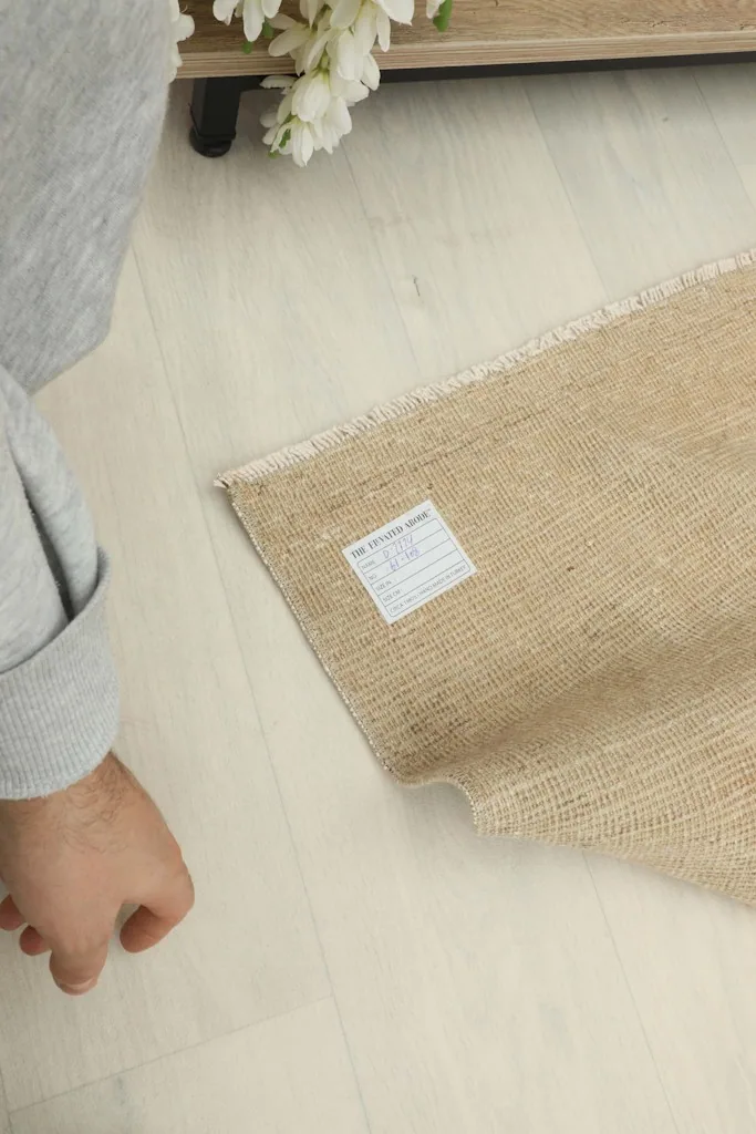 Hand touching the rug to illustrate scale and texture, with the product label visible on the back