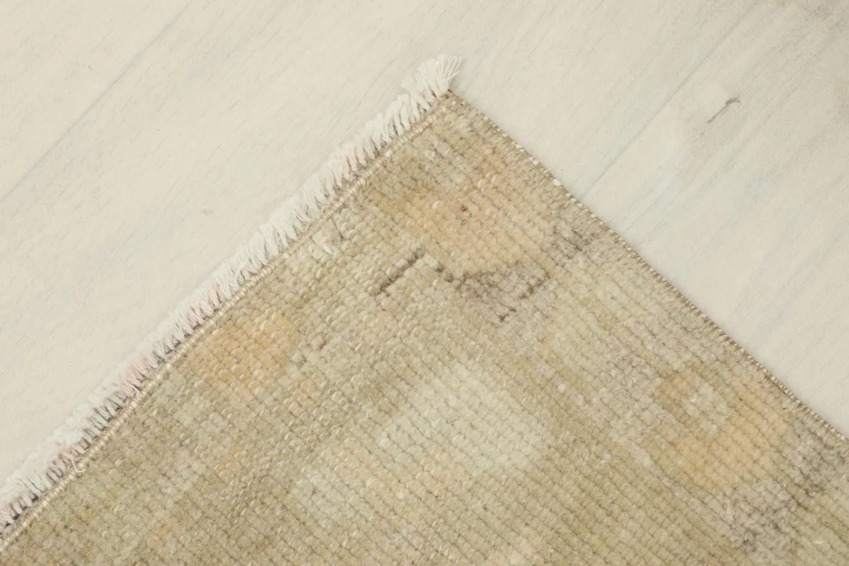Corner view of the vintage rug, showing the distressed beige and tan colors and soft fringe
