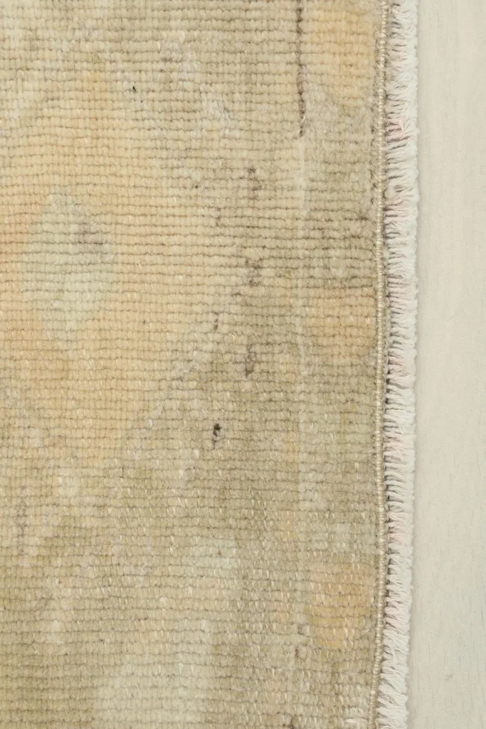 Close-up detail of the rug's beige wool pile and faded geometric design near the fringe