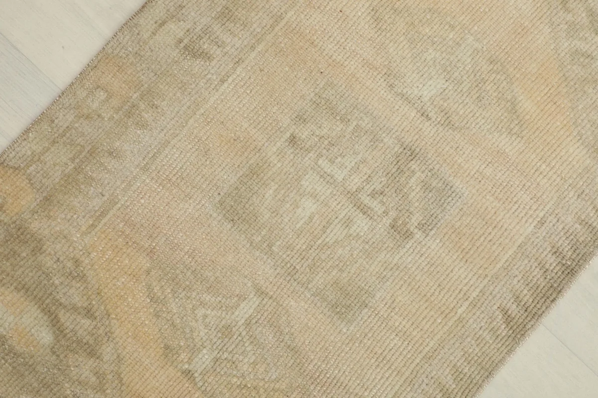 Angled close-up showing the subtle, faded geometric motifs within the distressed beige pile