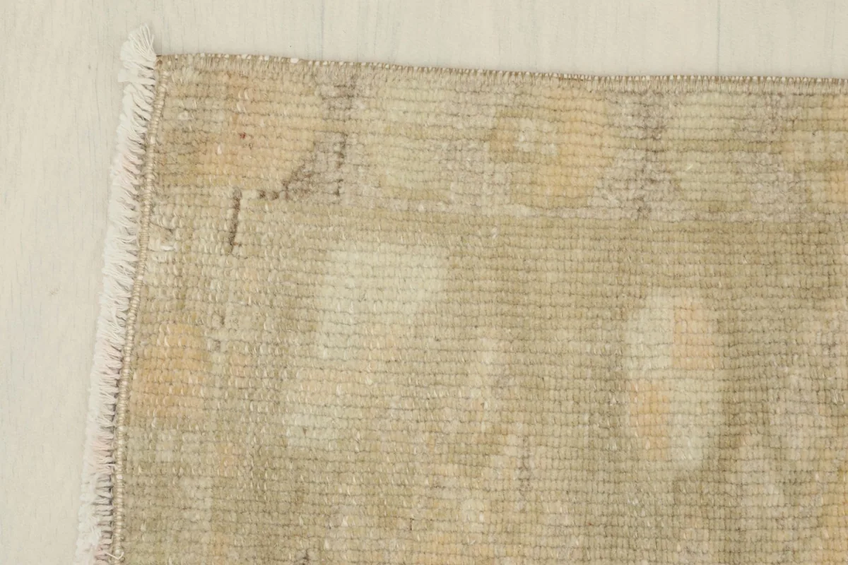 Close view of the rug's edge and fringe, revealing the hand-knotted texture and muted colors