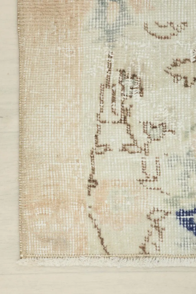 Close-up of the rug's edge, showing the faded beige tones and the short, neat fringe