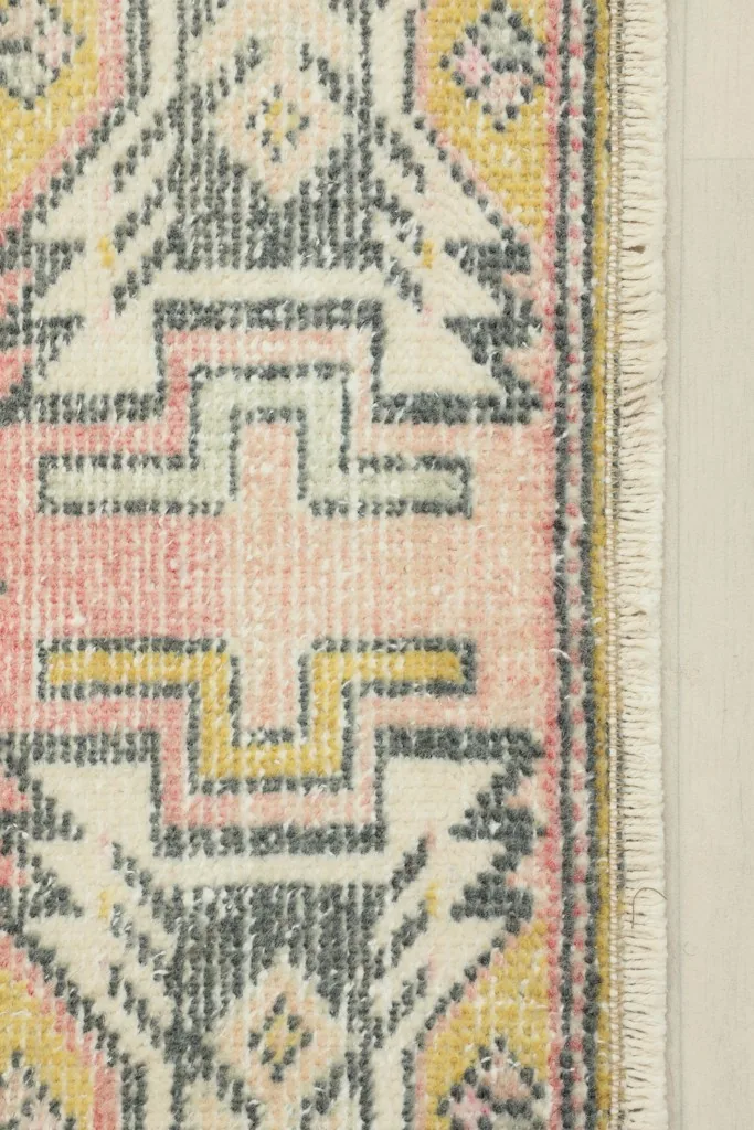 Close-up detail of the pink and yellow geometric border and fringe of the rug