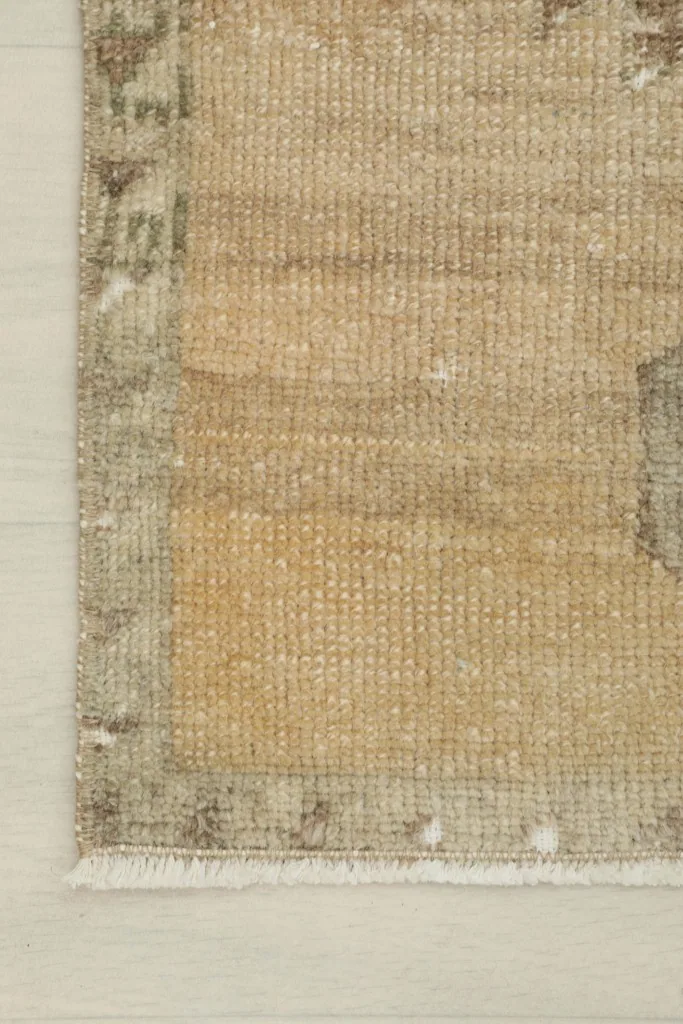 Detail of the rug's tan field and the subtle gray border with signs of wear.