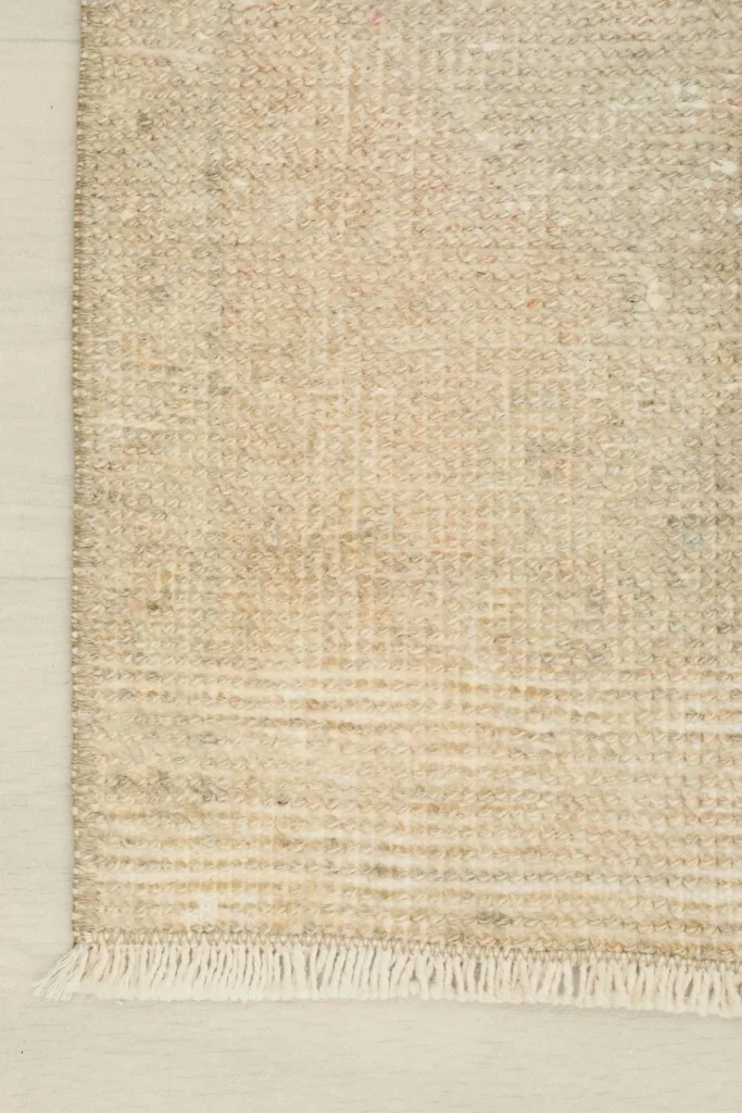 Close-up of the rug's edge and fringe, showing the weave and the natural wear on the wool pile.