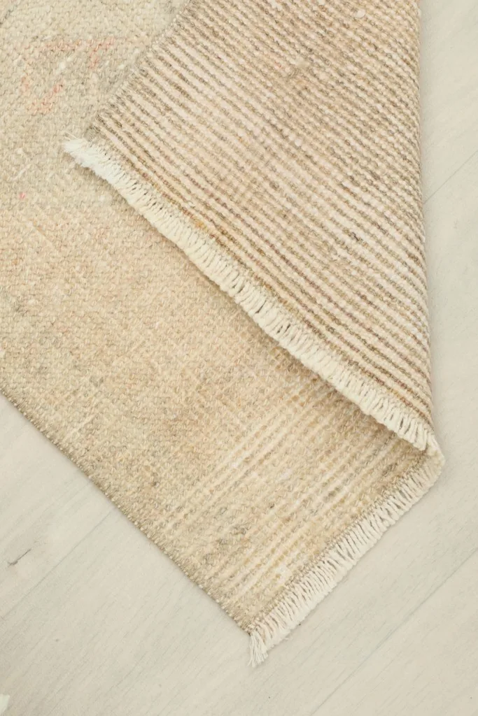 Rug corner folded back, showing the back of the hand-knotted cotton foundation and the wool pile front.