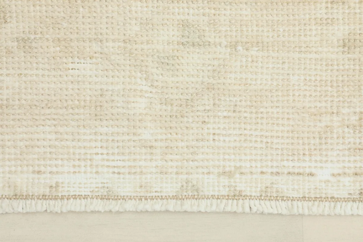 Close-up detail of the rug's low wool pile and subtle geometric texture in ivory and beige.