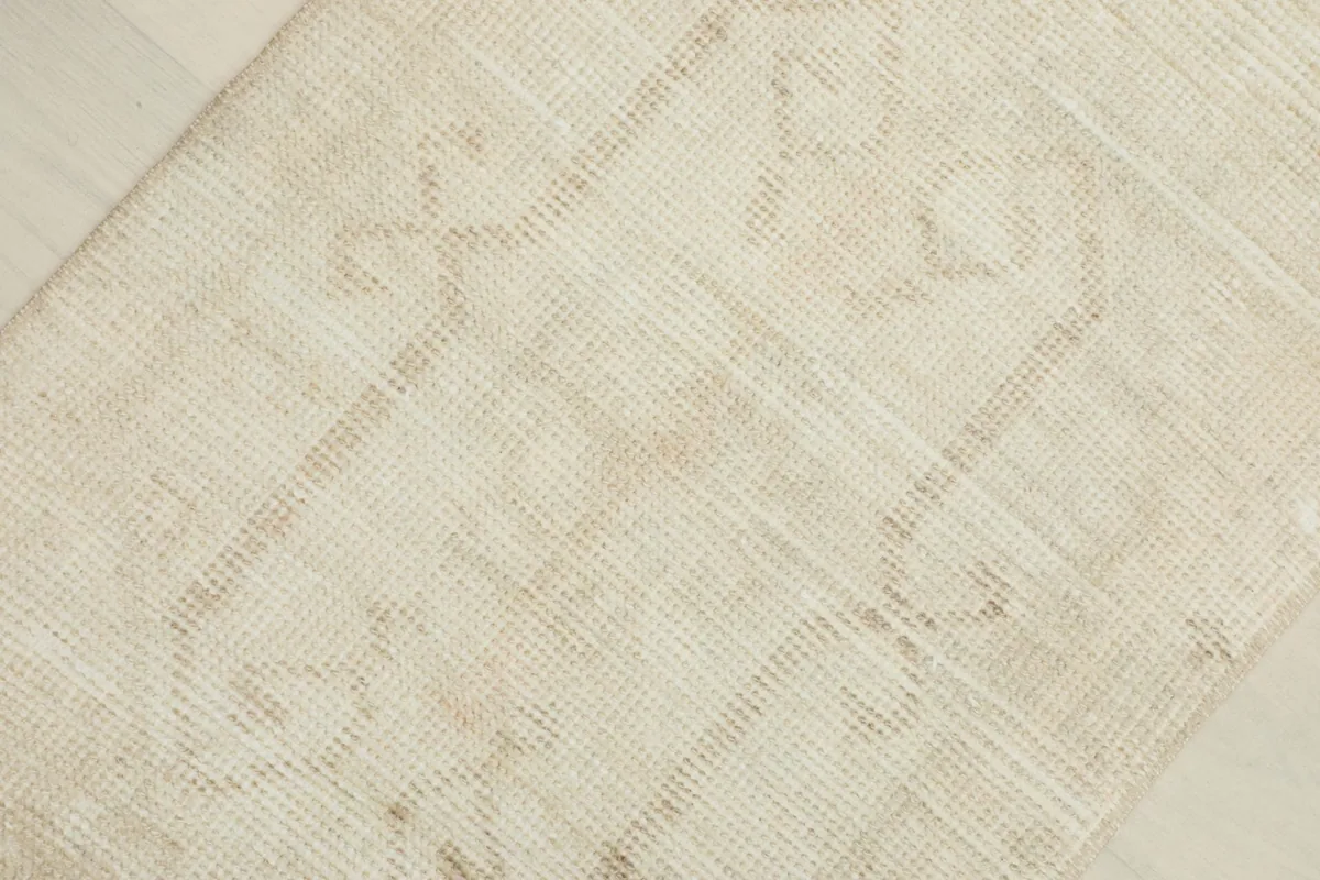 Detailed view of the rug's central area, revealing the faded geometric pattern within the ivory and beige field.
