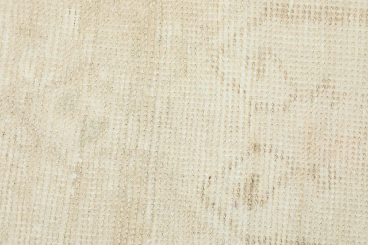 Macro shot of the low wool pile, showing the texture and muted color variations of the vintage rug.