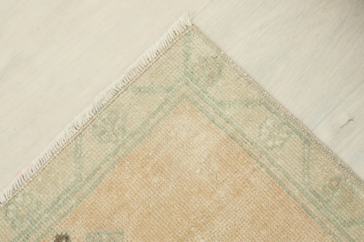 Corner view of the rug, displaying the green border and the short natural fringe.