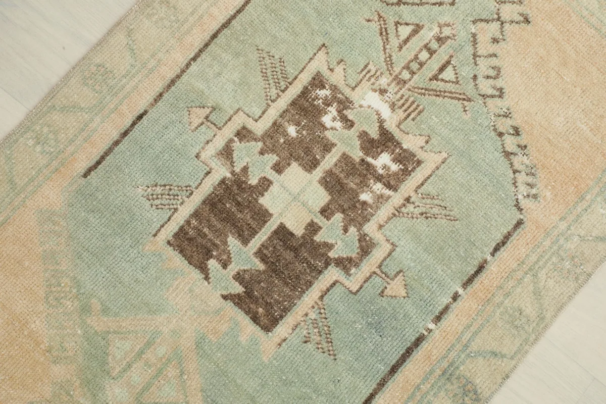 Detailed view of the central geometric motif in green and brown, highlighting its vintage character.