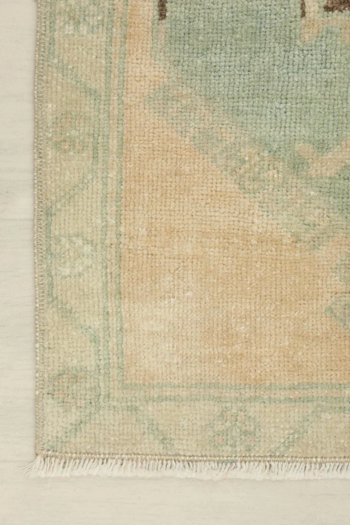 Close-up of the beige field and the green border design, showing the hand-knotted texture.