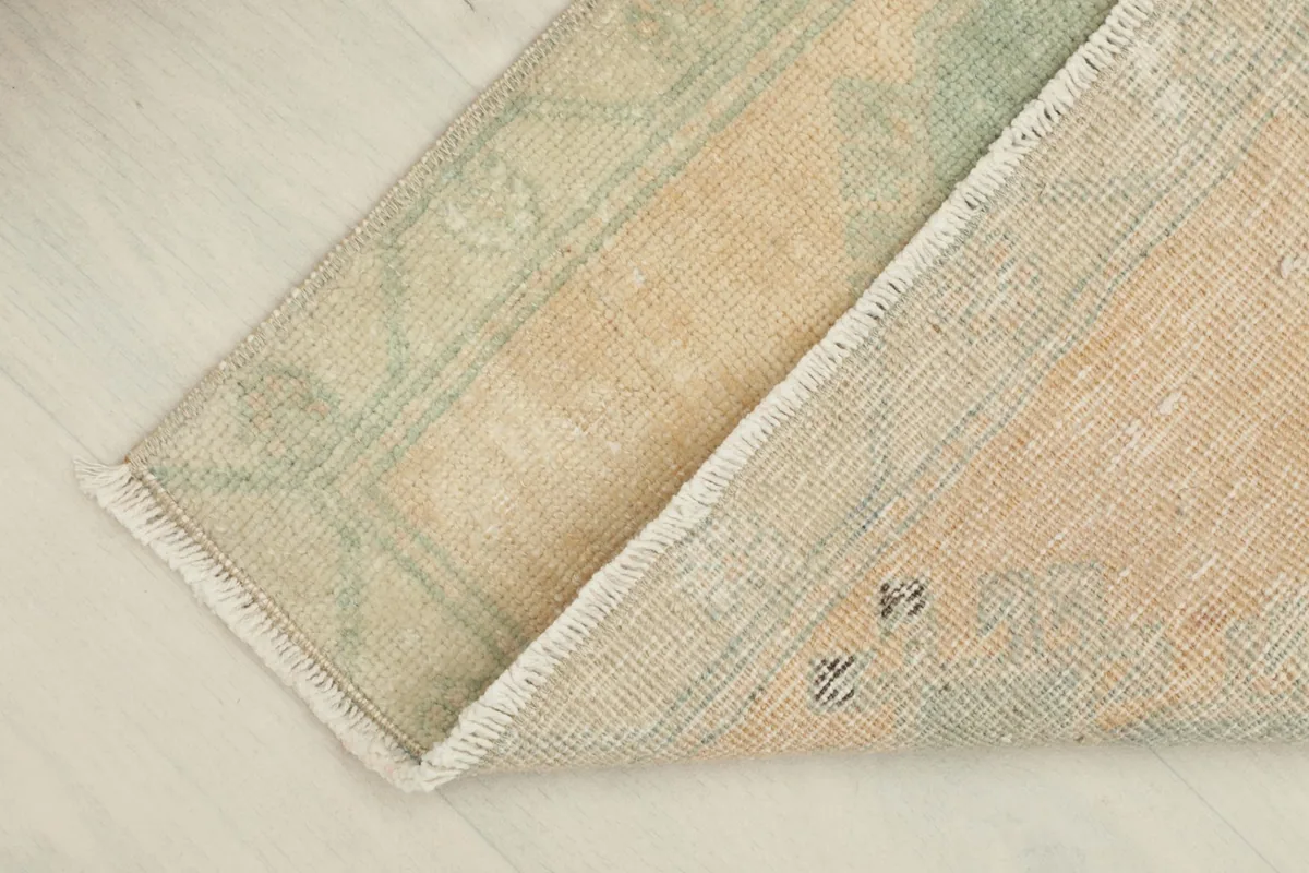 View of the back of the vintage wool rug, showing a small fold and the cotton foundation.