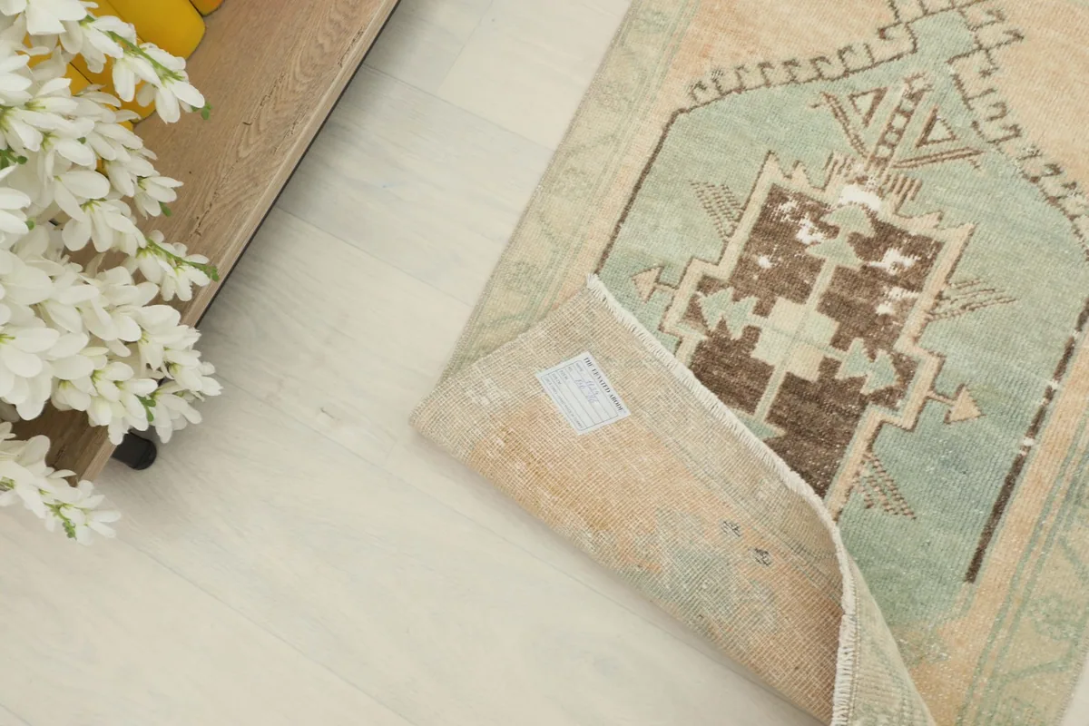 Back of the rug with a partial fold, showing the reverse side of the beige and green design.
