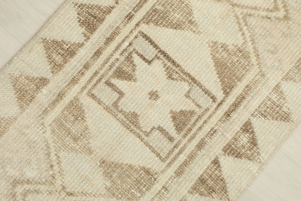 Detailed view of the central brown geometric motif and surrounding tribal patterns within the cream rug.