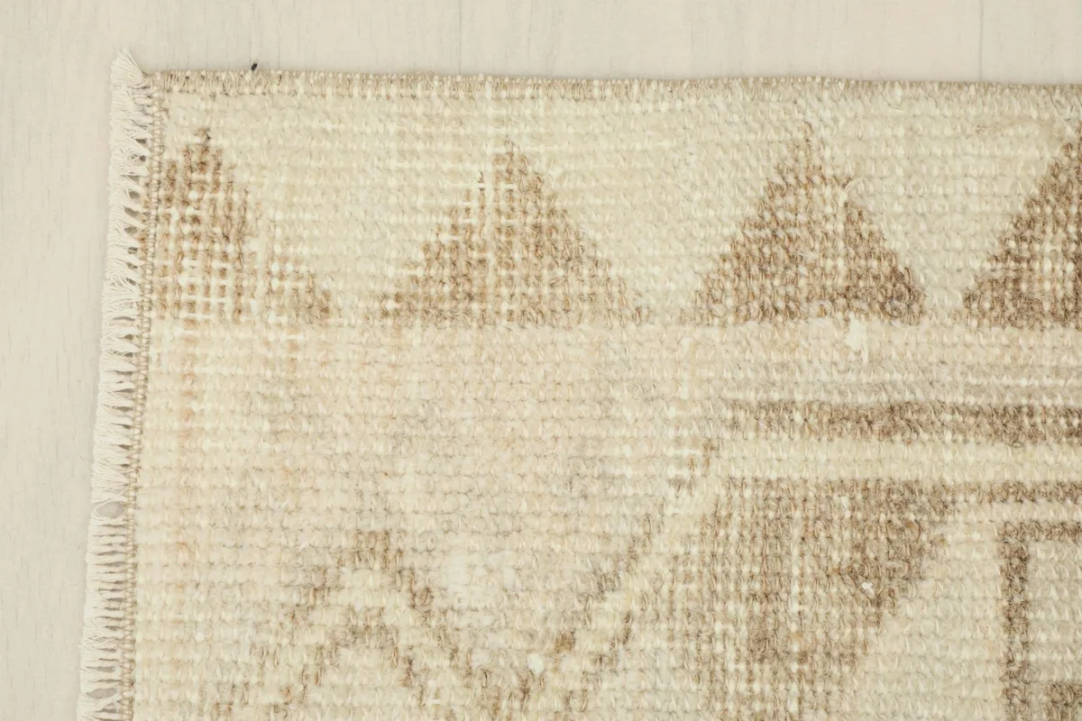Side border detail of the vintage rug, showing the consistent geometric triangles in brown against the cream.
