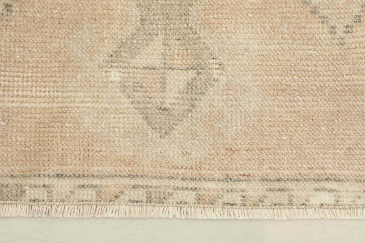 Close-up of the short fringe and the subtle geometric border pattern on the vintage rug.