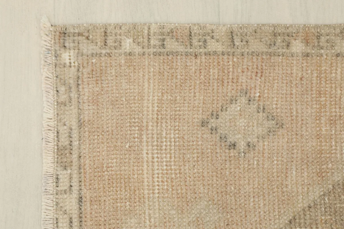 Corner detail of the rug, highlighting the faded rust field and the narrow, patterned border.