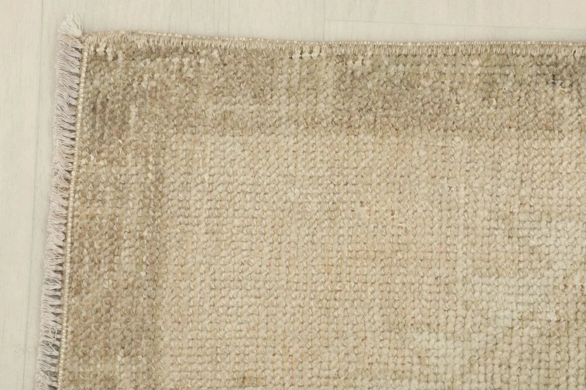 Detail of the rug's border and corner, showing the contrast between the beige field and tan border.