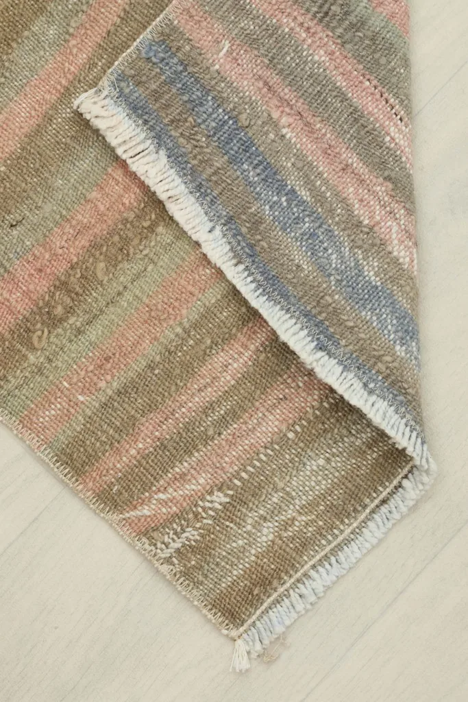 View of the rug folded to reveal the underside, showing the reverse side's construction and colors.