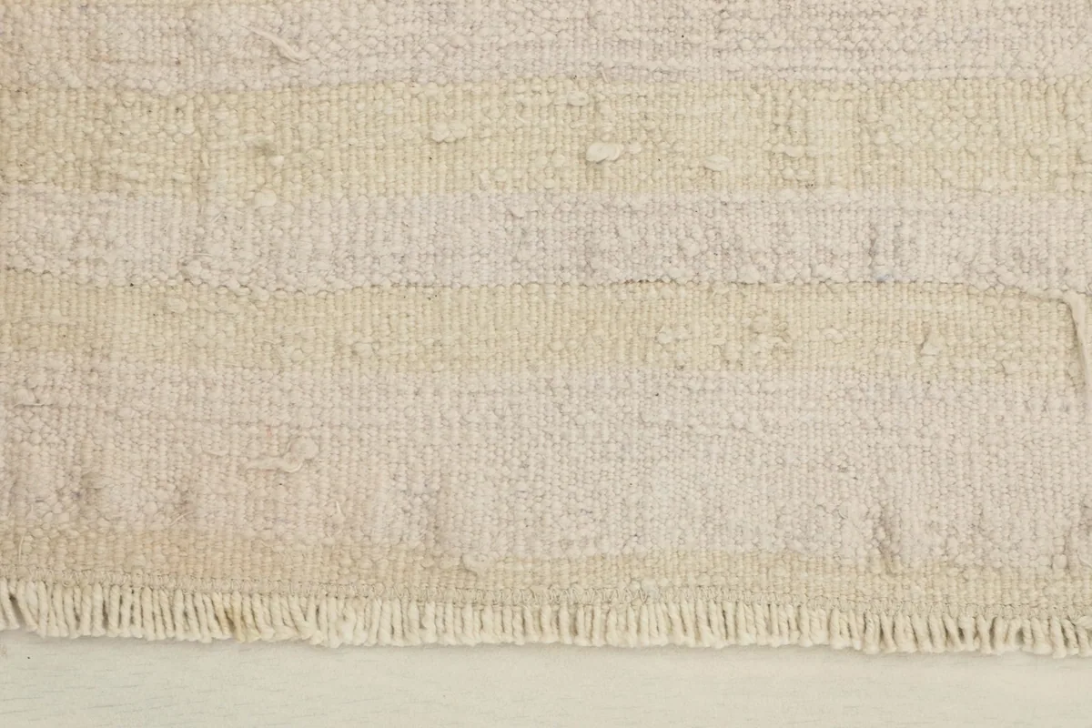 Close-up of the rug's texture, showing varied ivory and beige bands and the short fringe.