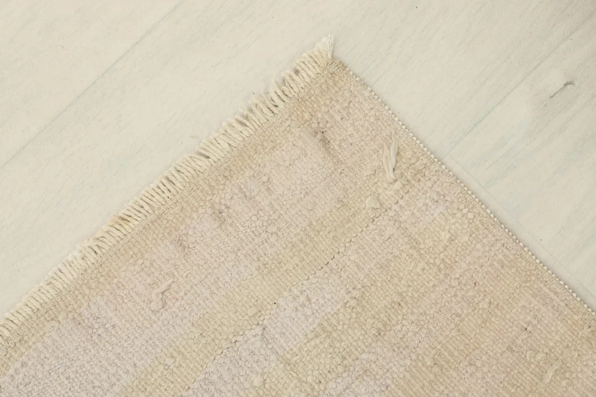 Overhead view of a corner of the rug, displaying its flat profile and light color palette.