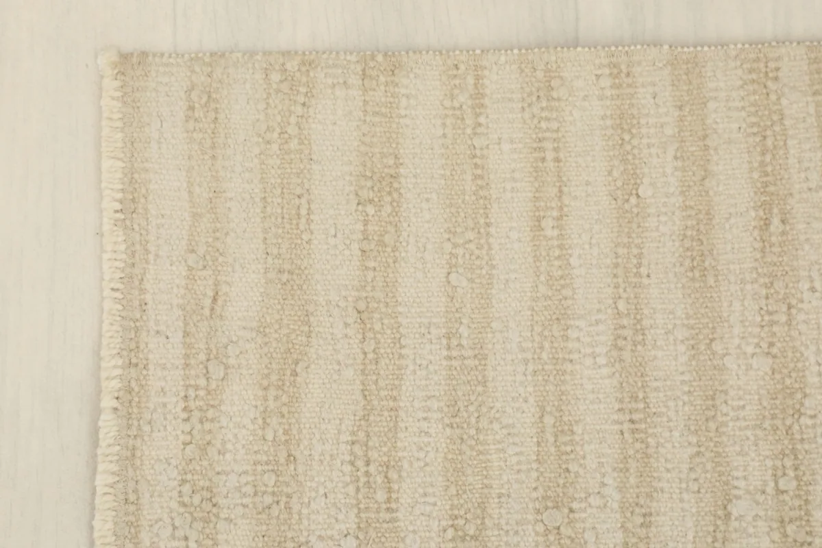 Corner detail of the beige striped rug, showing the subtle variations in the wool pile.