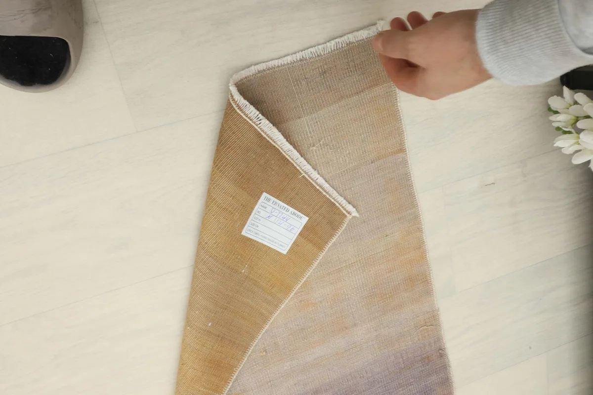 A hand holding a corner of the rug, displaying the thickness and the label on the back.
