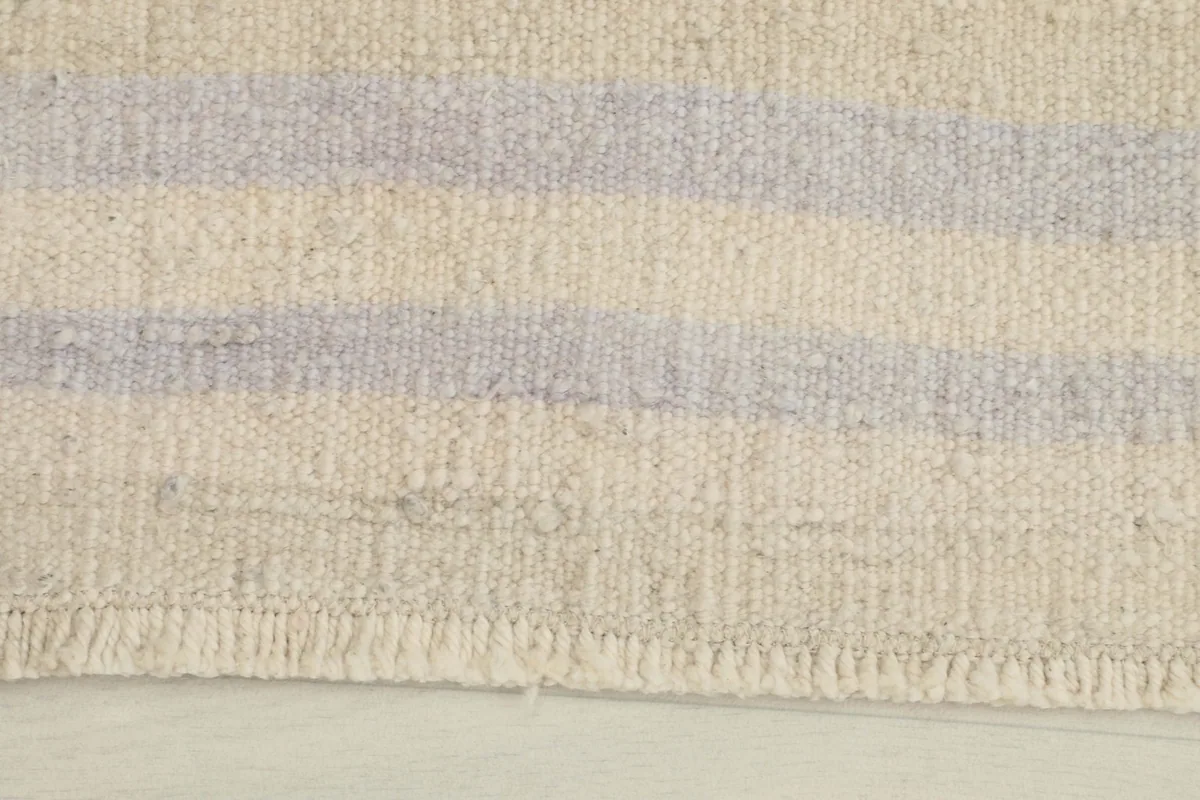 Close-up of the rug's edge, showing the texture of the ivory and purple wool pile and short fringes.
