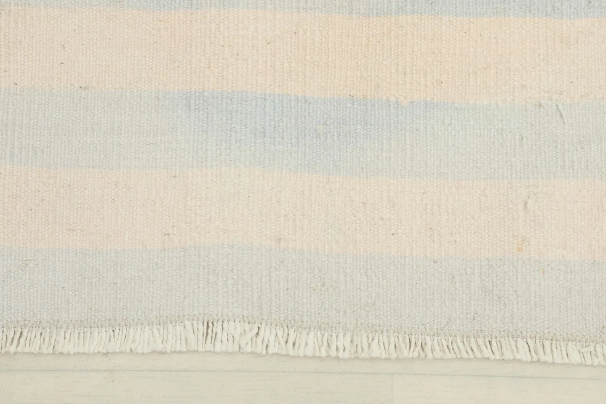 Close-up of the cream and blue stripes and fringe on one end of the rug.