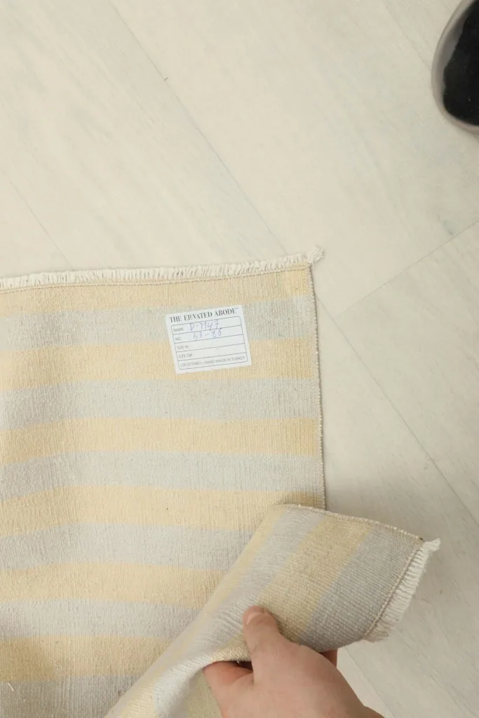 Hand holding a corner of the rug, showing the back label and striped pattern.