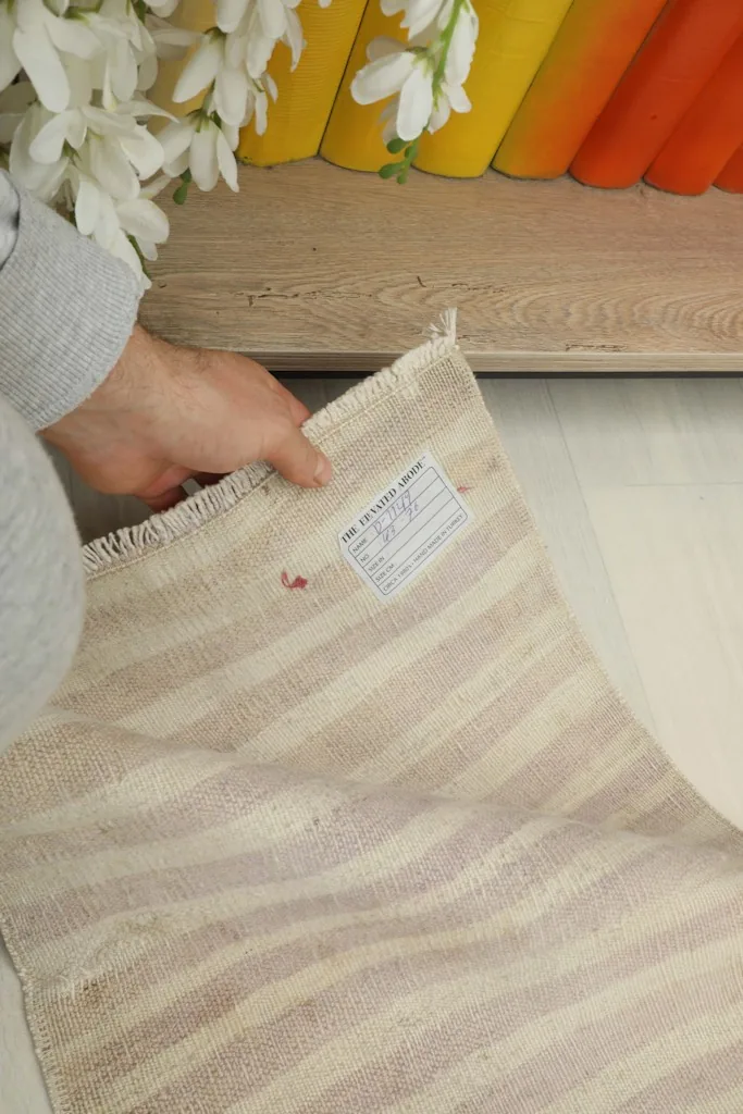 A hand holding the rug, showing the back with a label and the striped cotton foundation
