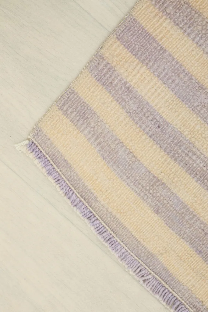 Corner view of the rug, showing the fringe and the striped pattern extending to the edge on a light floor.