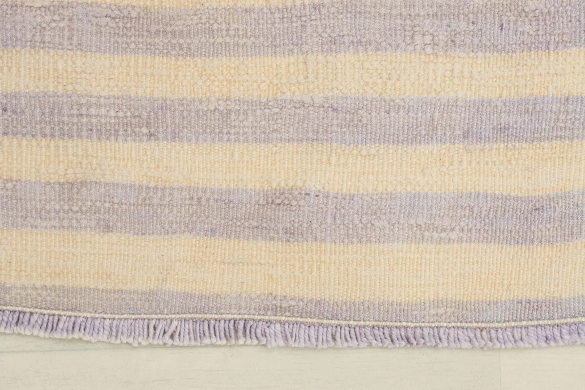 Close-up view of the rug's short fringe and the purple and ivory striped pattern along one edge.