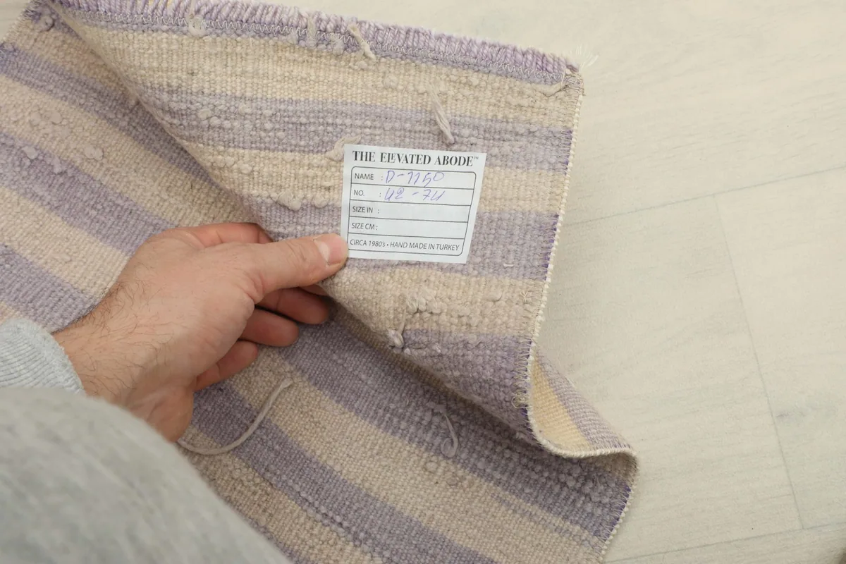 A hand holding a label on the back of the rug, showcasing the hand-knotted cotton foundation.
