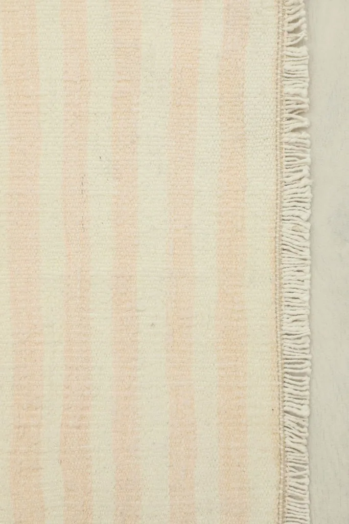 Close-up detail of the cream and rose stripes and the fringe along one edge of the hand-knotted rug.