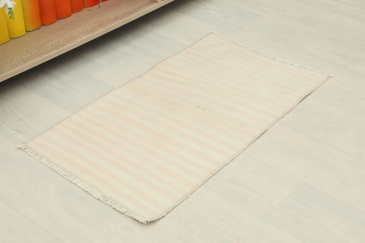 Slightly angled overhead view of the cream and rose striped doormat, showing its placement potential.