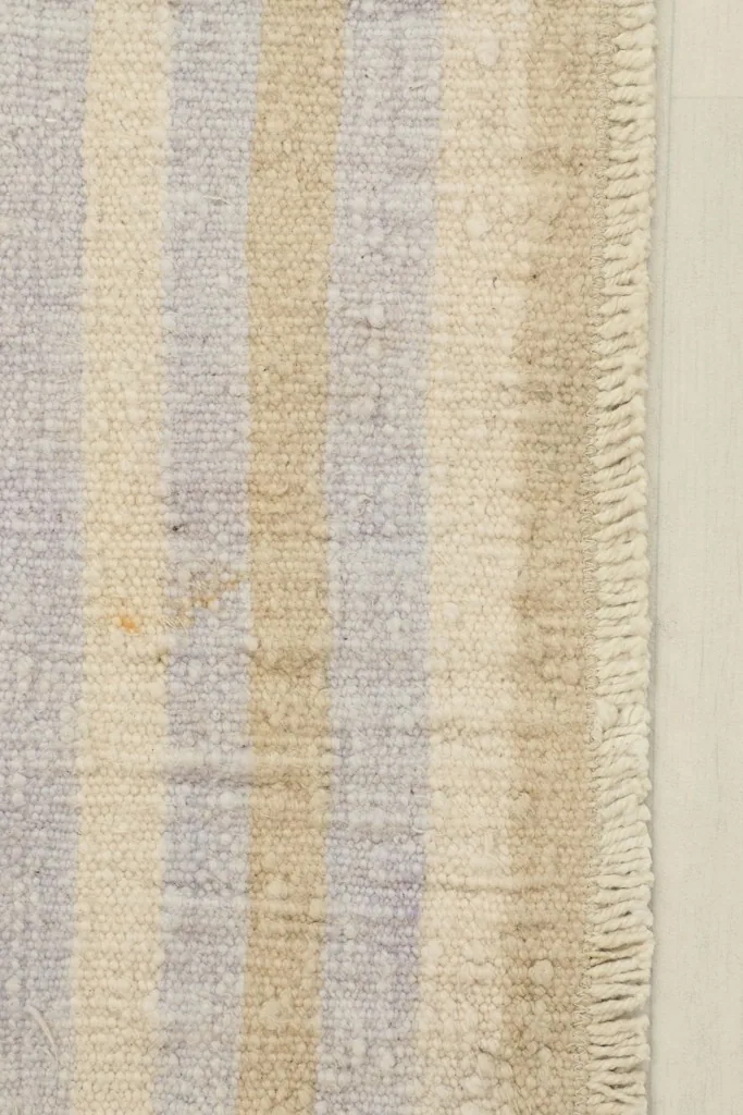 Close-up detail of the rug's striped pattern, showing beige and purple wool threads and fringe.