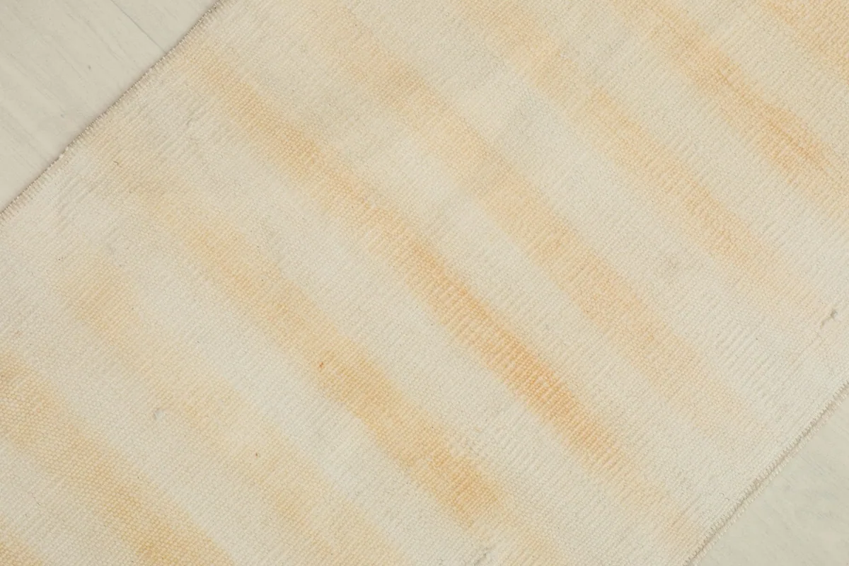 Diagonal close-up showing the texture of the low wool pile and the faded tan stripes on a cream field.