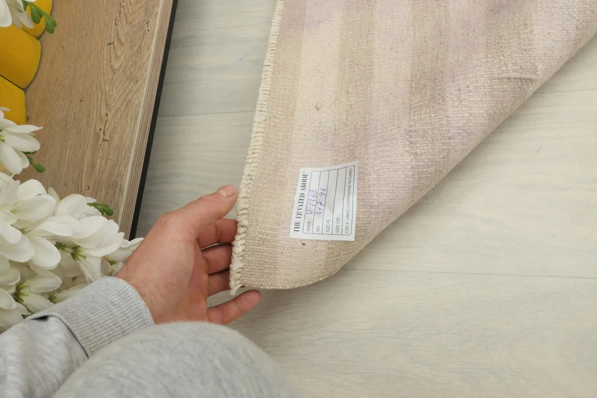 A hand lifting the rug to show the back side with a label, indicating its origin and material.