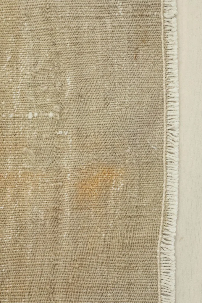 Close-up detail of the rug's low pile texture, showing the woven wool and cotton foundation with a hint of rust patina.