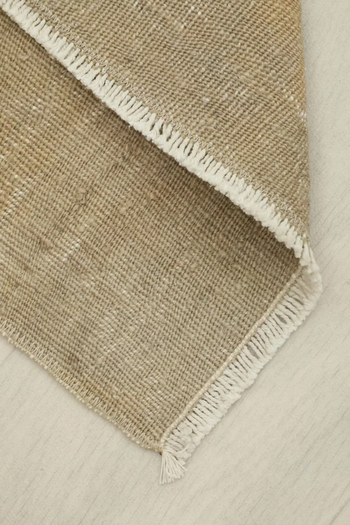 View of the rug folded back on itself, revealing the reverse side and the hand-finished edges.