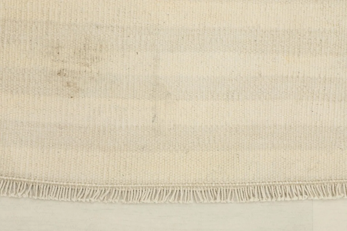 Close-up detail of the rug's short fringe and the tightly woven wool pile with horizontal ivory and beige stripes.