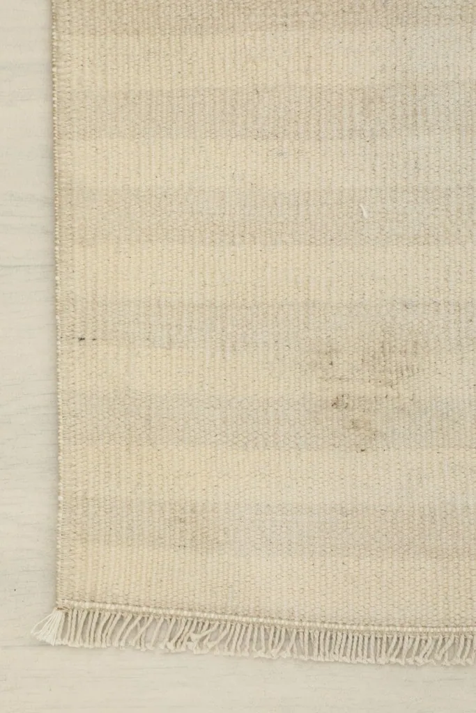Detailed view of the rug's edge, showing the hand-knotted texture and the natural variations in the ivory and beige tones.